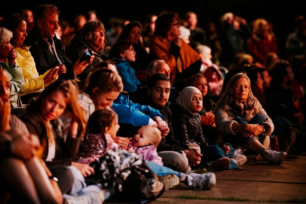 People relaxed on blankets and cushions in the grass, enjoying an evening of music and togetherness.